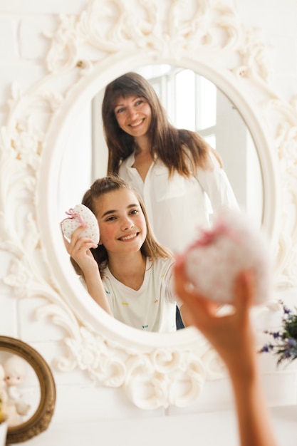 Riflessione della madre e della figlia sorridenti con il contenitore di regalo della tenuta