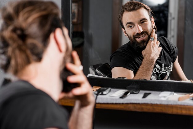Riflessione di un cliente maschio che governa la sua barba in specchio
