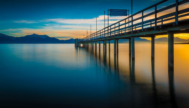 Riflessione di un molo di legno sul mare con le montagne e l'alba