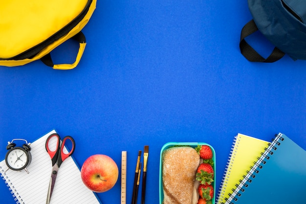 Rifornimenti di scuola e scatola di pranzo su fondo blu