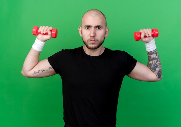 Rigoroso giovane uomo sportivo che indossa il braccialetto che si esercita con il dumbbell isolato sul verde