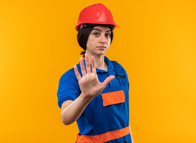 Rigoroso guardando la telecamera giovane donna del costruttore in uniforme che mostra il gesto di arresto