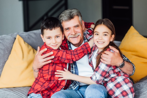 Rilassare. Felice nonno allegro che sorride e si siede sul divano con i suoi nipoti e li abbraccia.