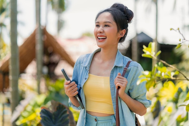 Rilassati casual spensierato sorridente asiatico femmina nomade digitale programmatore freelance tenere in mano laptop camminare sulla spiaggia e albero di cocco blu skynew stile di vita millenario lavorando ovunque con felicità