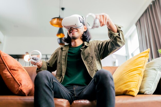 Rilassati casual uomo adulto asiatico che indossa le cuffie per realtà virtuale e tiene i controller Gioca in uno sport Videogioco a casa Gioca a VR gioco di sport attivo online nel soggiorno