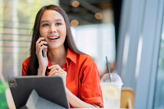 Rilassati per il tempo libero attraente imprenditore freelance asiatico femminile sorridente e divertiti a lavorare con smartphone e laptop al bar con il concetto di idee casual nomadi digitali di affari della città sfocata