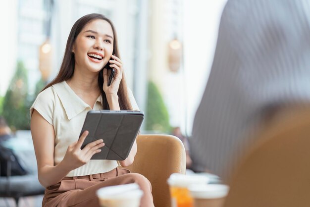 Rilassati per il tempo libero attraente imprenditore freelance asiatico femminile sorridente e divertiti a lavorare con smartphone e laptop al bar con sfocatura città affari nomade digitale lavoro a distanza idee casual concetto