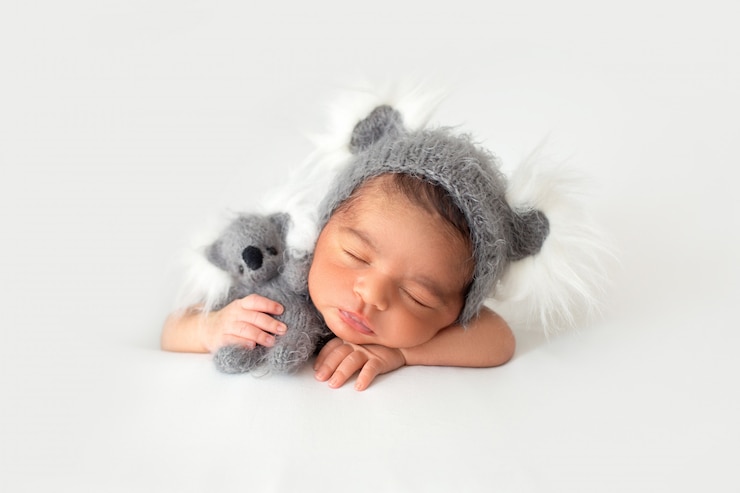 Foto gratuito riposo appena nato nel piccolo cappello grigio carino e con l'orso giocattolo grigio nelle sue mani