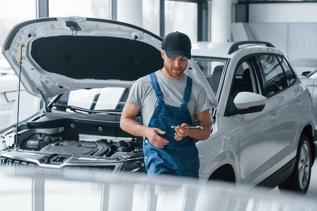 Riposo sul posto di lavoro. L'impiegato nell'uniforme di colore blu sta nel salone dell'automobile