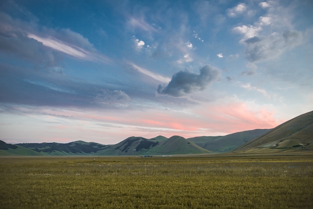 Ripresa a tutto campo di bellissime montagne verdi in un campo in erba sotto il cielo nuvoloso colorato in Italia