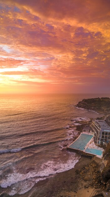 Ripresa aerea di una spiaggia con una grande piscina di un hotel e il mare durante il tramonto