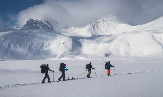 Ripresa orizzontale di un gruppo di persone che fanno un'escursione sulle montagne coperte di neve sotto il cielo nuvoloso