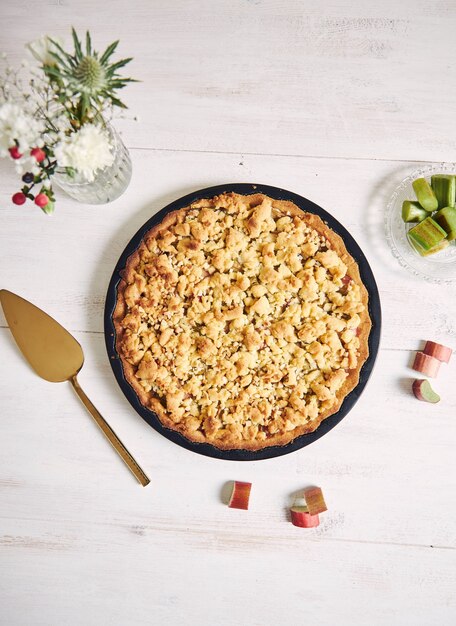 Ripresa verticale ad alto angolo di un piatto di crostata di torta Rhabarbar croccante e alcuni ingredienti su un tavolo