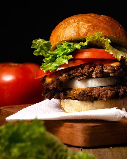 Ripresa verticale di un delizioso hamburger su un piatto di legno con una parete nera