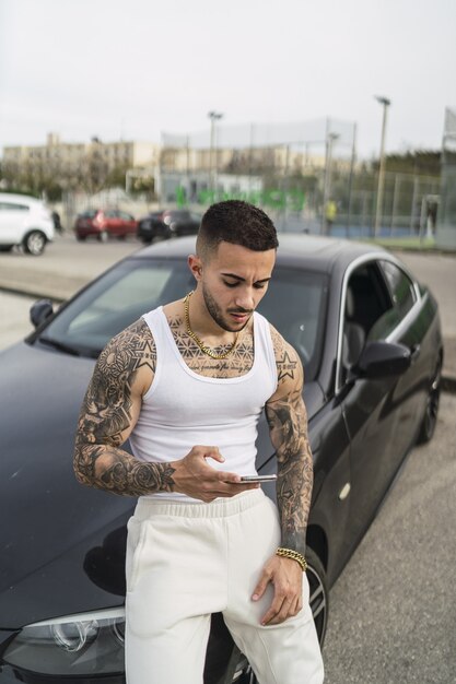 Ripresa verticale di un uomo tatuato sexy che usa il telefono appoggiato alla sua auto