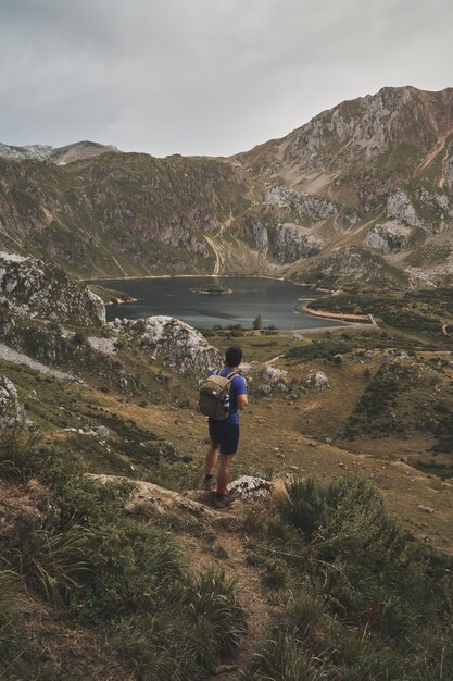 Ripresa verticale di un viaggiatore con zaino e sacco a pelo maschio che guarda un bellissimo lago nel Parco Naturale di Somiedo in Spagna