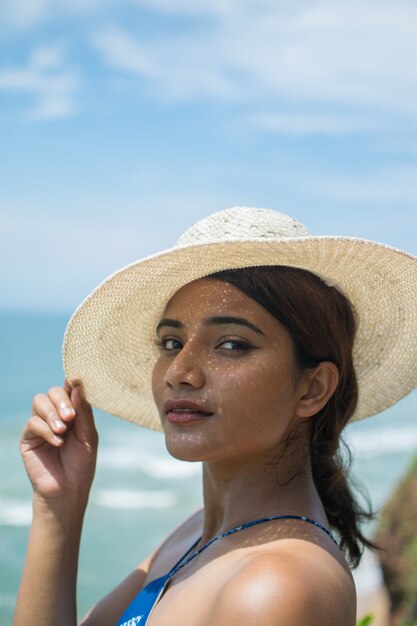 Ripresa verticale di una bella donna asiatica con cappello e costume da bagno sulla spiaggia