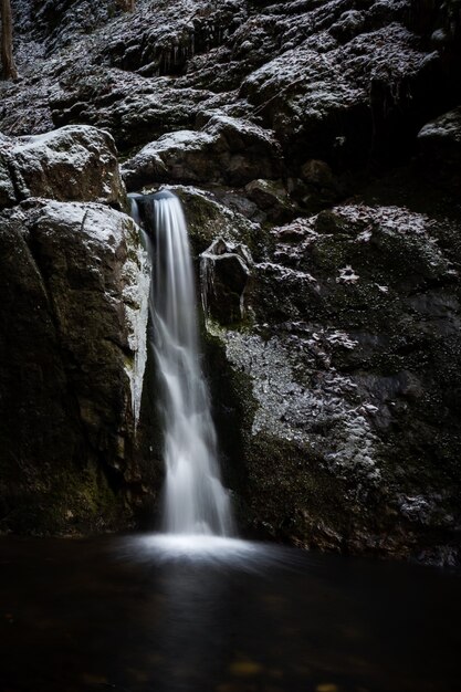 Ripresa verticale di una cascata che esce da un'enorme roccia coperta di neve nella stagione invernale winter