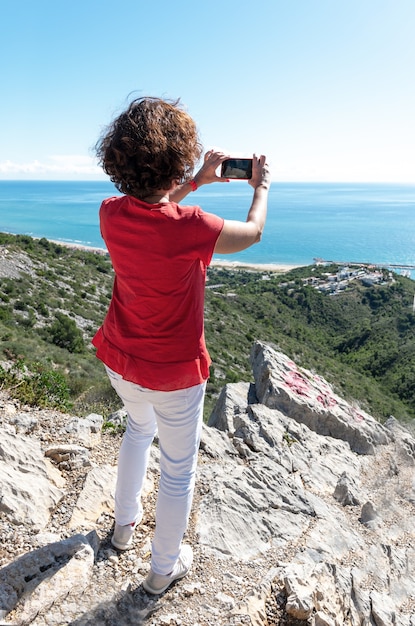 Ripresa verticale di una donna in piedi sulle rocce e che fotografa il bellissimo mare