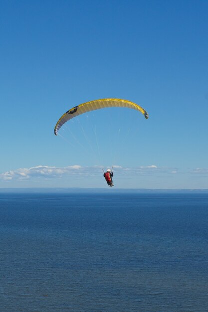 Ripresa verticale di una persona che vola in parapendio sopra il mare sotto la luce del sole