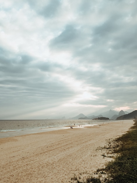 Ripresa verticale di una spiaggia circondata dal mare sotto un cielo nuvoloso a Rio de Janeiro, Brasile