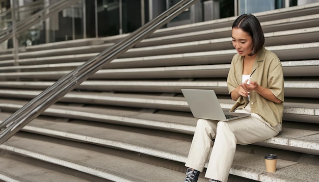 Ripresa verticale di una studentessa asiatica che partecipa a una riunione online parlando alla chat video del laptop seduta su