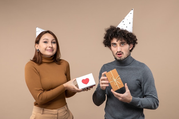 Riprese di Capodanno con coppia giovane divertente emotiva indossare ragazza cappello di Capodanno con cuore e ragazzo con regalo su grigio