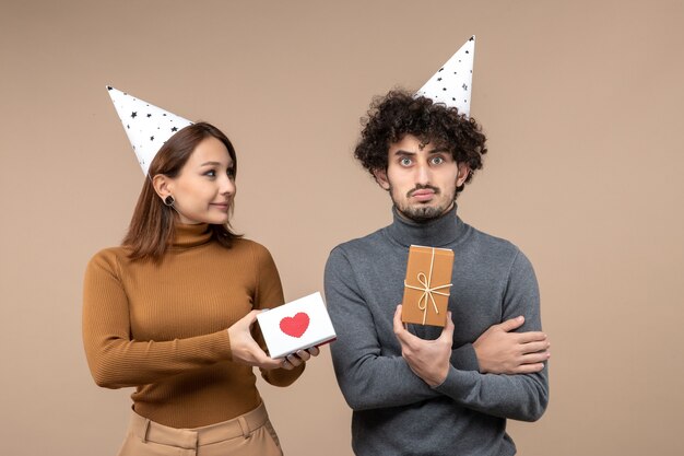 Riprese di capodanno con giovane coppia indossare cappello di capodanno ragazza romantica con cuore e ragazzo triste con regalo su grigio