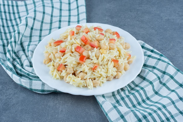 Riso al vapore con piselli e fette di pomodoro sul piatto bianco.