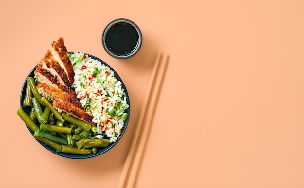 Riso con spezie, salsa di soia e spicchi di tacchino in una ciotola nera con fagiolini fritti, peperoncino e spezie. Preparato in un wok. Vista dall'alto con copia spazio. Idea di cibo asiatico