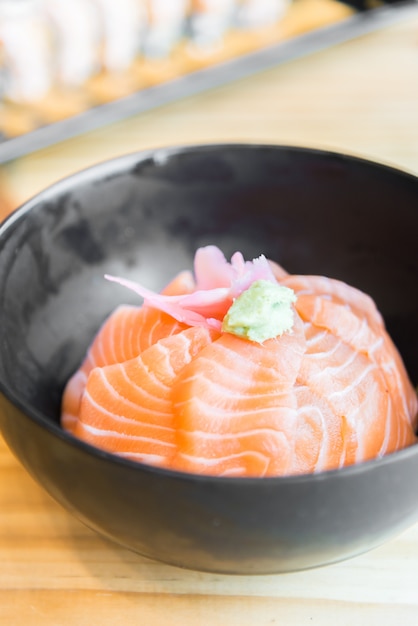 Riso giapponese con sashimi di salmone in cima in ciotola nera