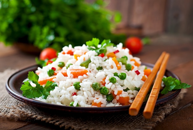 Riso sano appetitoso con le verdure in piatto bianco su una tavola di legno.