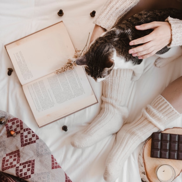 Ritaglia il gatto petting donna vicino a libro e cioccolato