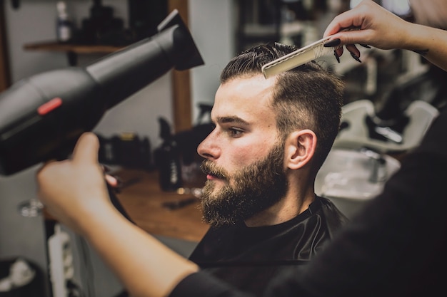 Ritaglia la donna che asciuga i capelli dell&#39;uomo nel negozio di barbiere