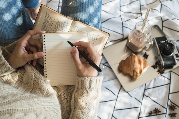 Ritaglia la donna che fa le note vicino alla macchina fotografica e al cibo della prima colazione