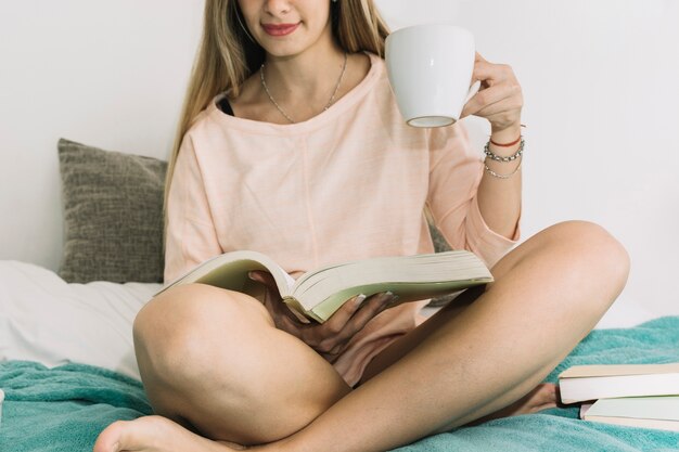 Ritaglia la donna con la tazza che legge sul letto