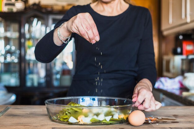 Ritaglia le mani della donna anziana che spruzza il piatto con sale