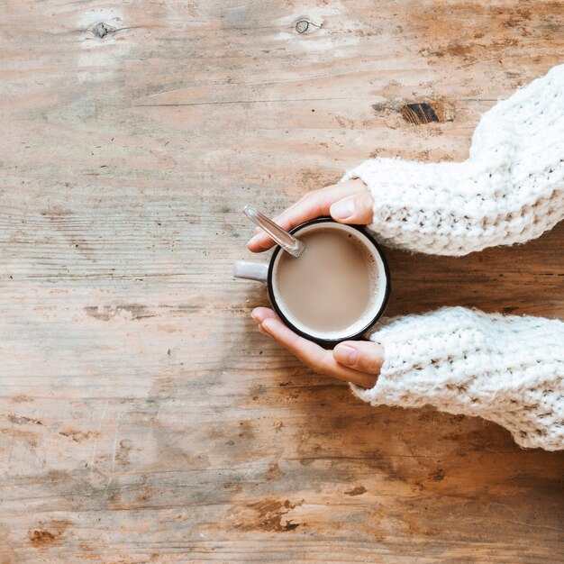 Ritaglia le mani nel maglione che scalda vicino al caffè caldo