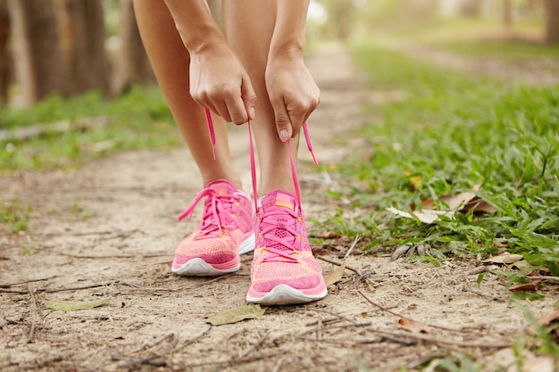 Ritagliata colpo di corridore di giovane donna che stringe i lacci delle scarpe da corsa, preparandosi per fare jogging all'aperto.