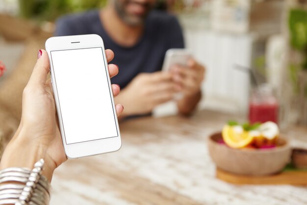 Ritagliata colpo di mano femminile che tiene il telefono cellulare con touchpad, utilizzando l'app online durante la colazione. Donna che legge un messaggio via e-mail, godendo della connessione internet gratuita al bar