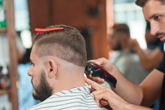 Ritagliata ravvicinata di un barbiere professionista che lavora presso il suo barbiere dando un taglio di capelli al suo cliente maschio.