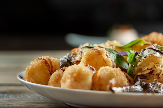 Ritagliata ravvicinata di un piatto pieno di palline di formaggio fritto sul tavolo di legno sul muro scuro copyspace piatto pasto delizioso gustoso nutrizione grassi calorie malsane.