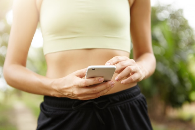 Ritagliata ritratto di giovane atleta femminile utilizzando il telefono cellulare durante l'esercizio all'aperto.