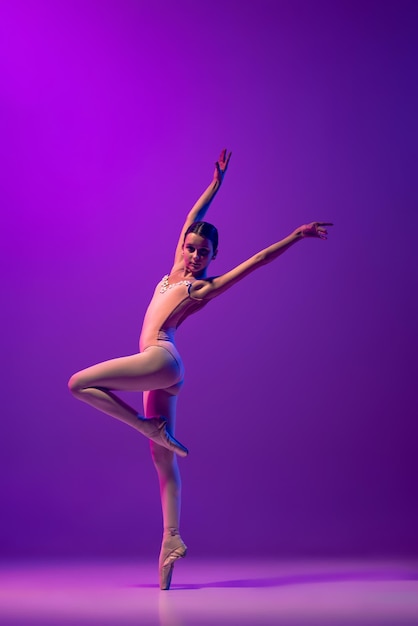 Ritratto a figura intera di giovane ballerina in pointe in piedi che balla isolato su sfondo blu viola sfumato al neon