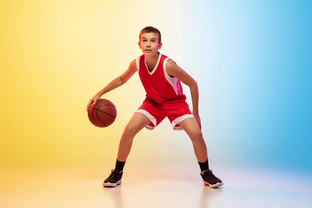 Ritratto a figura intera di un giovane giocatore di basket con palla su parete sfumata