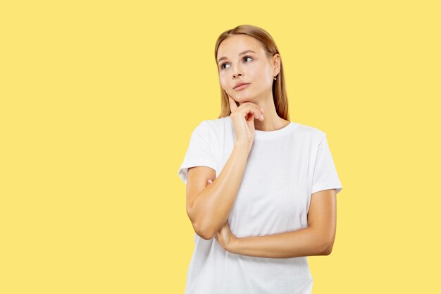 Ritratto a mezzo busto della giovane donna caucasica su sfondo giallo studio. Bello modello femminile in camicia bianca. Concetto di emozioni umane, espressione facciale. Sembra serio, premuroso.