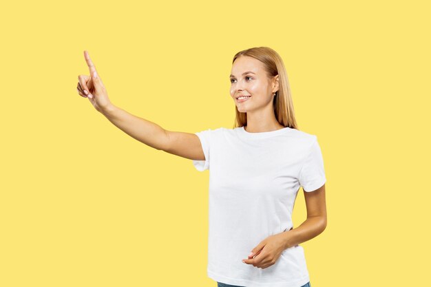 Ritratto a mezzo busto della giovane donna caucasica su sfondo giallo studio. Bello modello femminile in camicia bianca. Concetto di emozioni umane, espressione facciale. Toccando una barra di ricerca vuota e sorridendo.