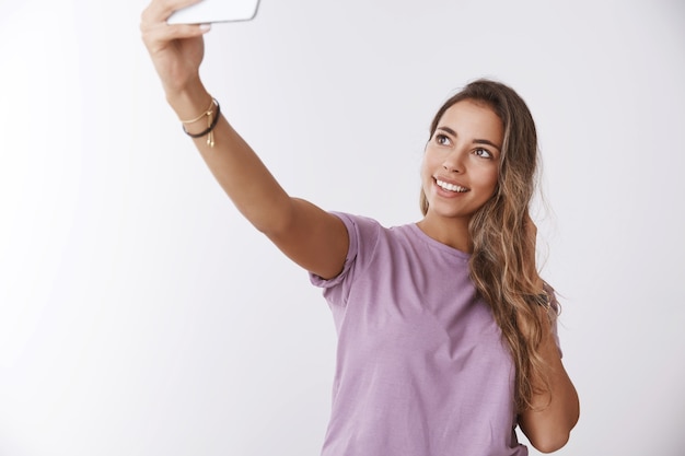 Ritratto affascinante ragazza felice viaggiatore visite turistiche prendendo selfie sorridente in posa muro bianco estendere la mano cattura foto dall'alto angolo, tenendo lo smartphone, condividendo foto di viaggio seguaci di internet