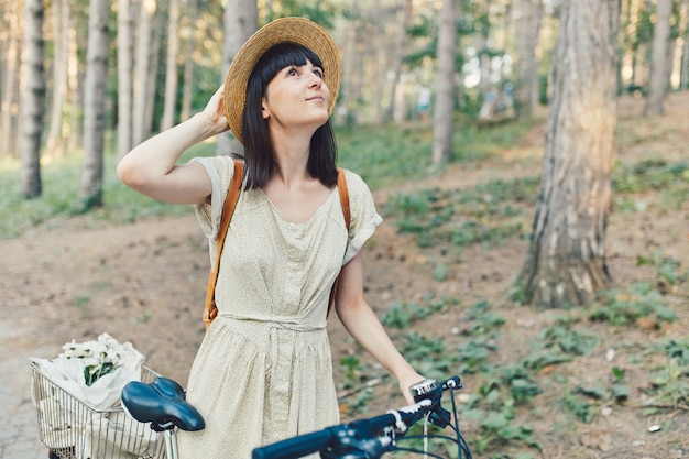 Ritratto all'aperto di giovane castana attraente in un cappello su una bicicletta.