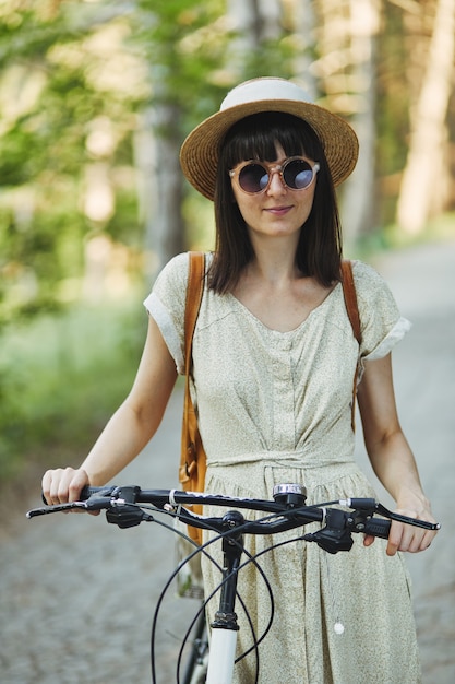 Ritratto all'aperto di giovane castana attraente in un cappello su una bicicletta.